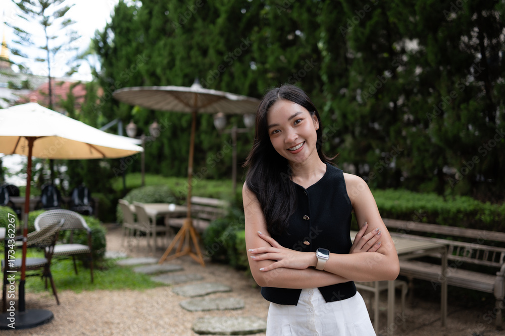 Naklejka premium Young Asian woman smiling confidently in outdoor cafe garden