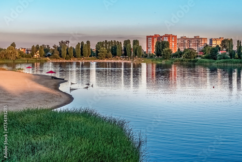 Evening view of Khorol River beach in Myrhorod resort town, Poltava region Ukraine, with calm water reflections, sandy shore and Soviet-era apartment buildings backdrop