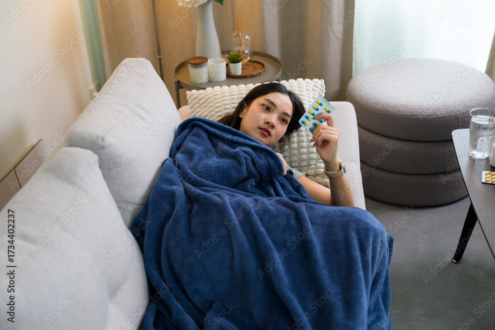 Obraz premium Sick woman lying on sofa holding medicine blister pack