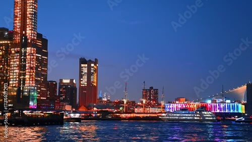 Fantastic illumination of the buildings and streets at the waterfront of the East River. Diverse boats arrive to the pier at dusk time.