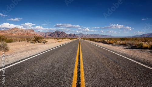 open desert highway stretches towards distant mountains under bright blue sky with scattered clouds asphalt road features double yellow line signifying direct path forward dry brush rocky hills