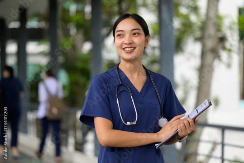 Photos Young Asian female nurse wearing scrubs holding clipboard