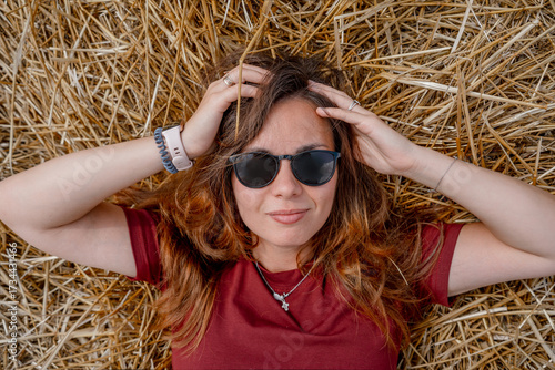 Fototapeta A young woman with blond hair lies on a haystack in summer, top view