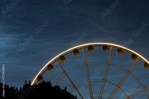 Illuminated Ferris wheel at night with bright cabins glowing against a dark blue sky filled with visible stars. 