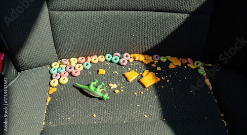 Messy back seat of a family car with spilled snacks cereal crackers crumbs and a toy dinosaur