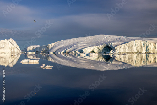 White iceberg perfectly reflected in the sea with blue sky above