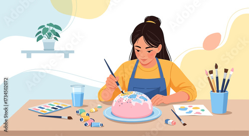 Creative young woman painting cake with a brush in a colorful home studio atmosphere