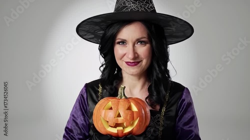 Woman In Witch Costume Holding Carved Pumpkin On Gray Backdrop