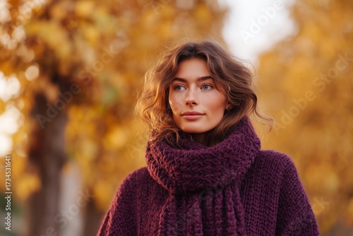 Woman in plum knit sweater walking through autumn park with falling leaves in golden light