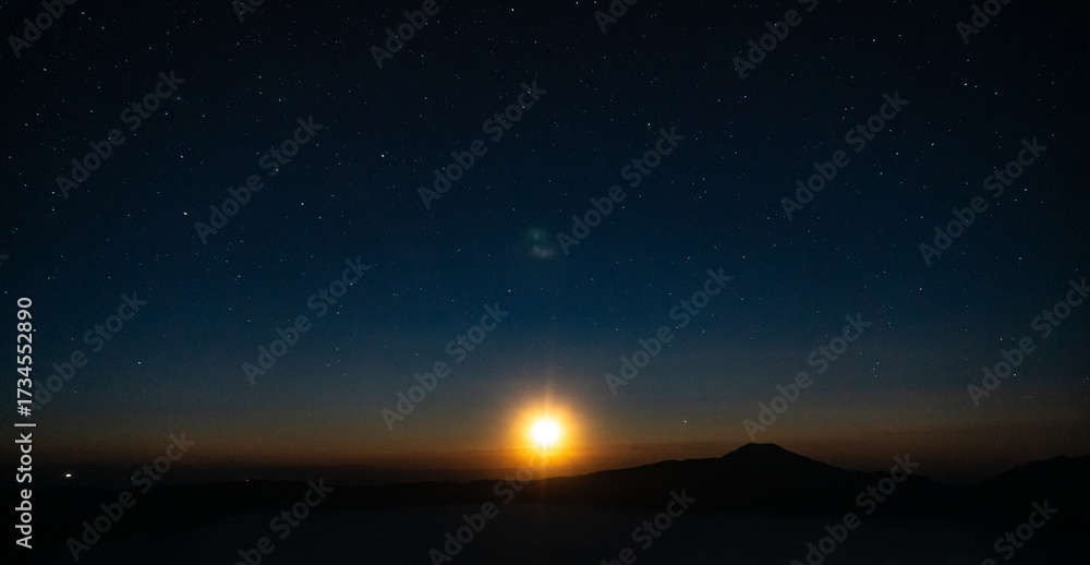 Fototapeta premium Night sky with stars and a bright light source near the horizon over a dark silhouette of land