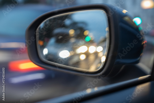 Blurry nighttime street reflection in a car side mirror showing approaching traffic headlights and a pedestrian, emphasizing urban travel and safety