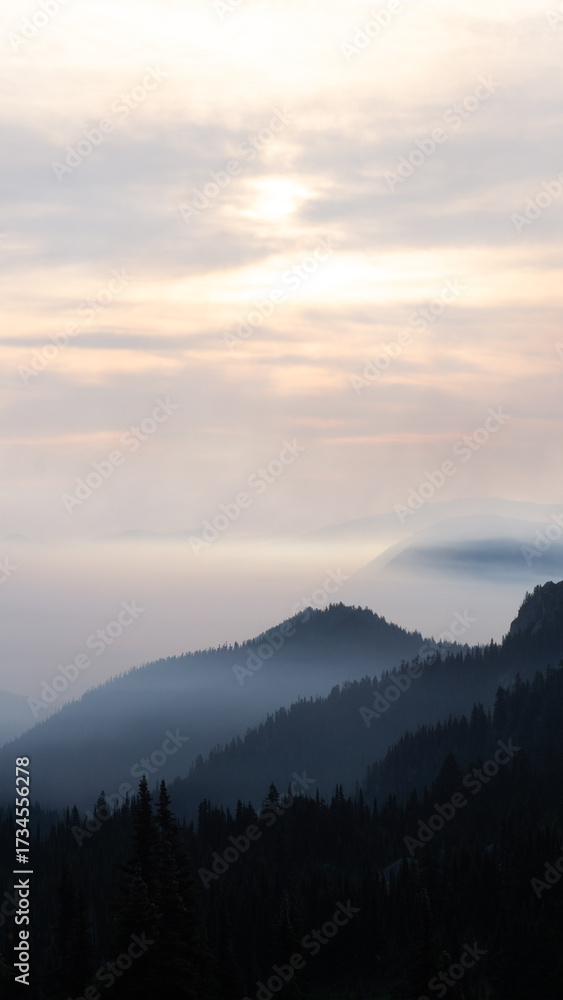 Obraz premium A scenic view of layered mountain ranges under a cloudy sky at dusk or dawn with a soft light glow