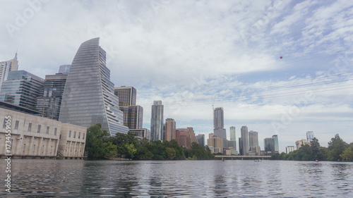 Modern city skyline viewed across a calm body of water, with skyscrapers reflecting on the surface under a cloudy sky. Represents urban lifestyle and development.
