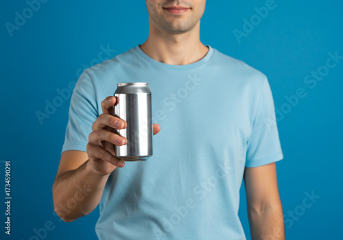 Refreshing drink concept, man offers a cool beverage in a sleek aluminum can against a vibrant blue backdrop, perfect for summer ads and promotions