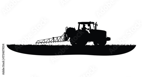 Silhouette of a tractor spraying crops on a grassy field