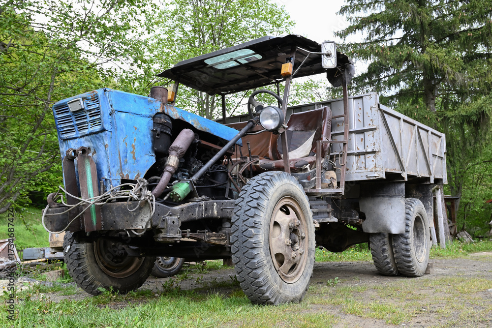 Fototapeta premium Old homemade farm vehicle with a blue tractor front and metal cargo bed, parked outdoors on a rural yard. Perfect for themes of farming, countryside, sustainability, recycling.