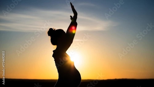Silhouette of a pregnant woman raising her arms in joy during sunset, with a serene landscape in the background