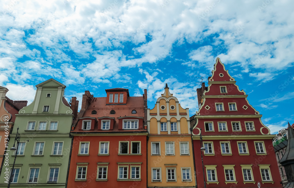 Fototapeta premium Vibrant facades of historic townhouses with decorative gables and white-trimmed windows line up beneath a dynamic sky, illustrating the architectural beauty of Wroclaw, Poland’s Old Town.