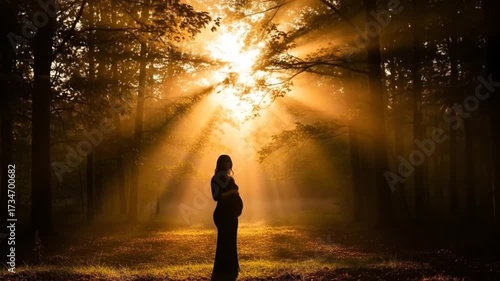 Silhouette of a pregnant woman standing in a sunlit forest, surrounded by trees and golden rays of sunlight