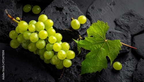 Fresh green grapes rest on dark stones, accented by a vibrant leaf, creating a beautiful still life.
