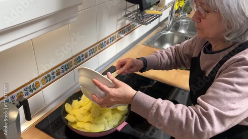 Senior woman with white hair frying potatoes in a pan for Spanish omelette