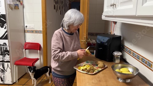 Senior woman with white hair peeling potatoes in kitchen preparing traditional Spanish omelette