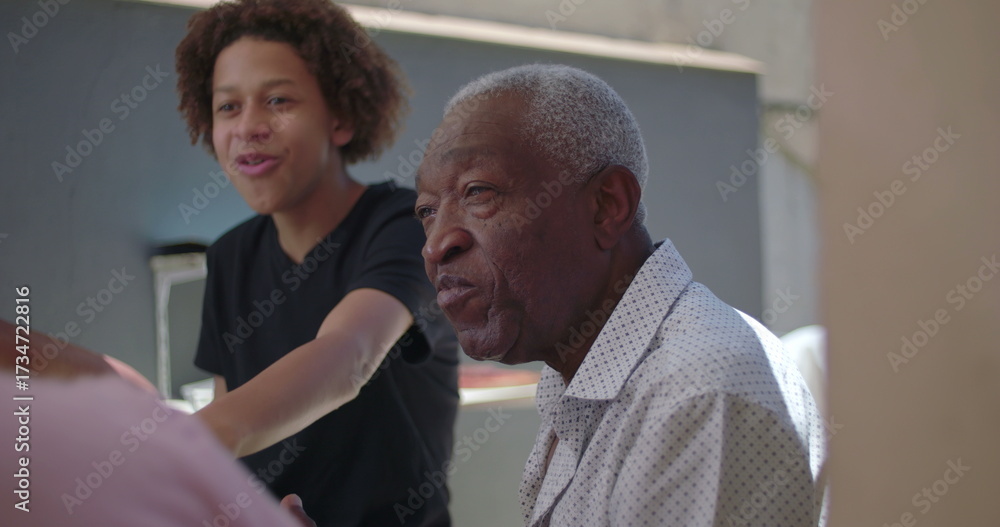 Obraz premium Teenager and grandfather sharing laughter during a family meal outdoors, highlighting generational connection, joy, and warmth in a diverse family setting