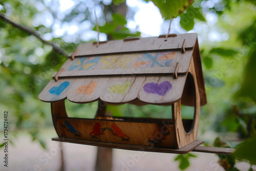A small, decorated birdhouse hangs outside from a branch with greenery in the background.