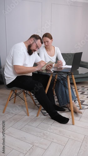 Young couple sitting at kitchen table, analyzing financial documents, calculating household expenses, sharing serious discussion about budgeting challenges, managing monetary stress together