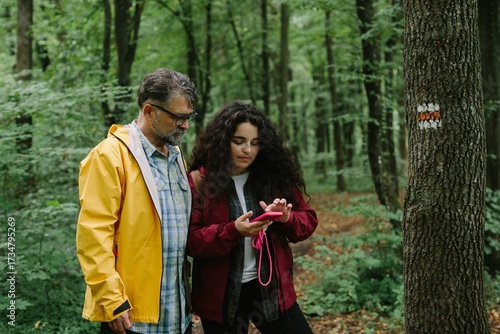 Картината върху платно Father and daughter navigating forest path using smartphone