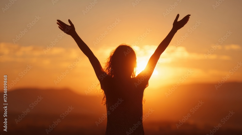 Fototapeta premium A figure stands with arms raised in celebration during sunset, surrounded by a breathtaking orange and yellow sky. The silhouette creates a feeling of joy at the days end.