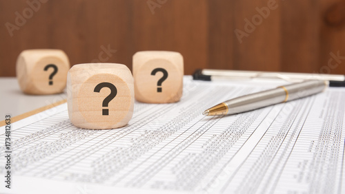 wooden cubes with black question marks on financial spreadsheet with pen and blurred background