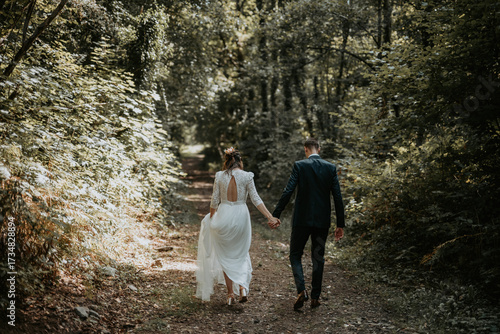 Un couple de jeune mariés qui marche ensemble dans une forêt en se tenant la main