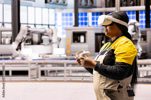 Automation engineer integrates virtual reality into manufacturing process at smart factory. Black female industry 4.0 worker uses VR headset and controllers to enhance training and troubleshooting.