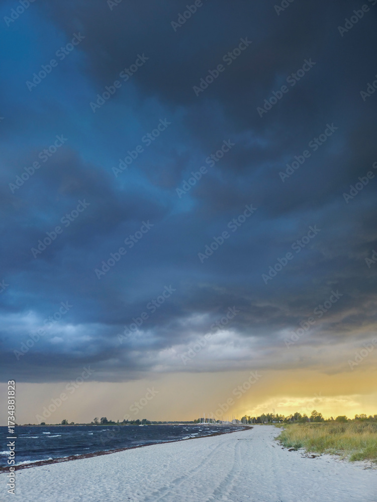 Obraz premium Dramatic coastal scene with stormy skies above a tranquil beach at sunset