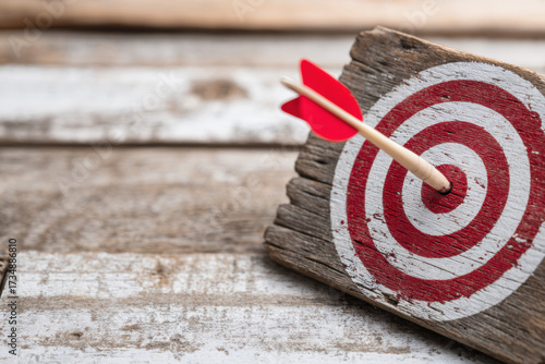 A wooden target with a red and white bullseye, hit precisely in the center by a single arrow.
