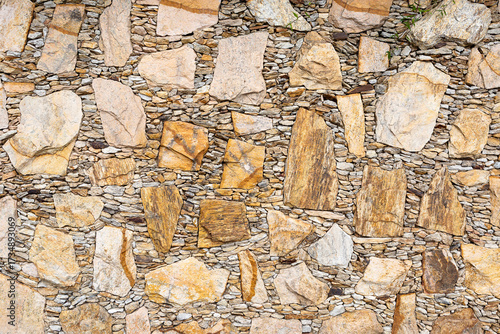 Close-up of rustic yellow stone wall with irregular shapes and small rocks filling the gaps. Perfect for backgrounds, architecture, and construction design concepts.