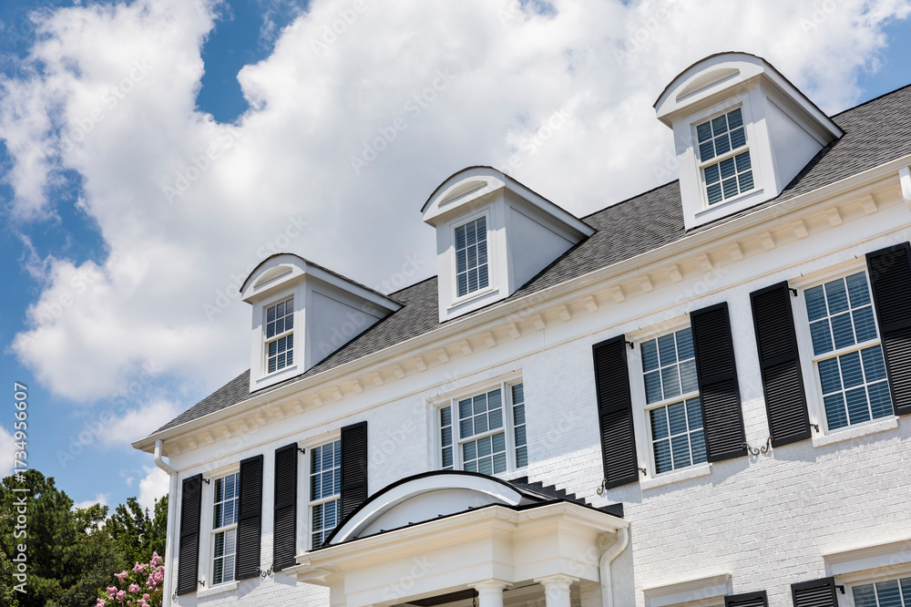 Obraz premium Exterior view of a modern suburban home with a white brick facade, gable roof, and large windows under a partly cloudy sky.