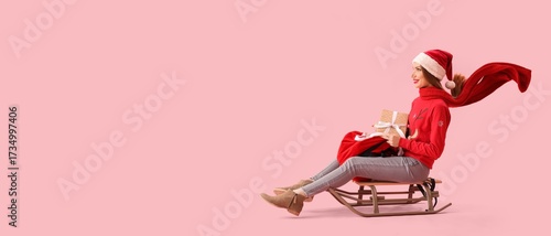 Fotografie Beautiful young woman in Santa hat and with bag of Christmas gifts sledging on p