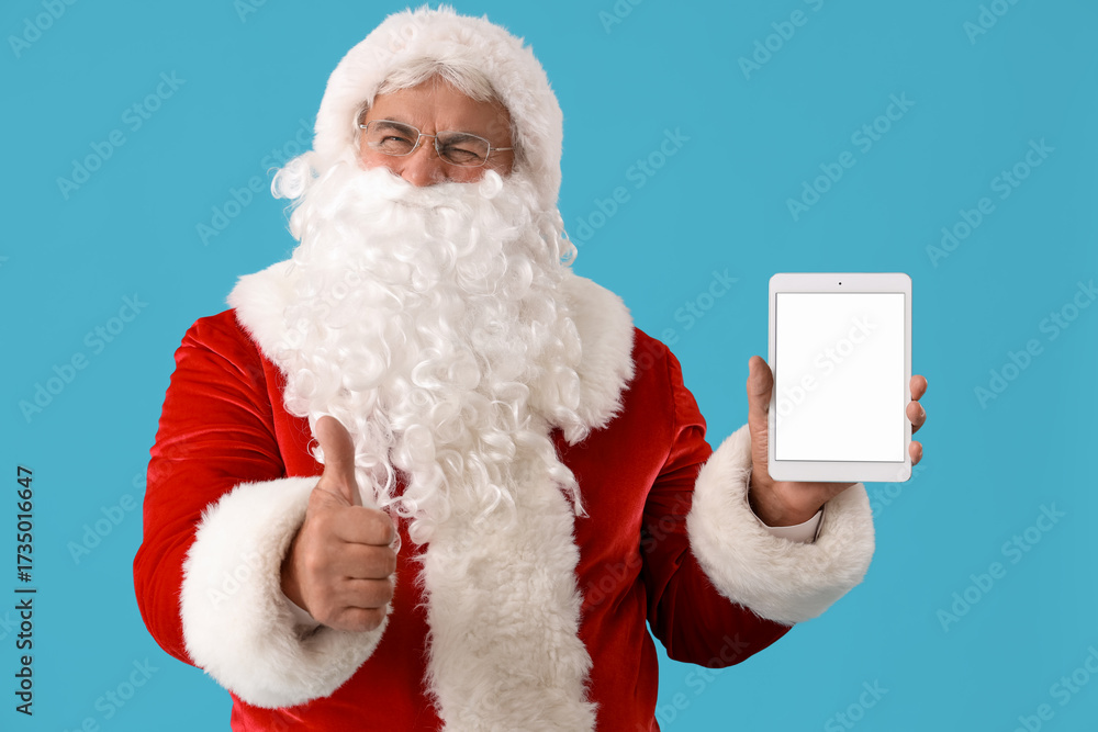 Naklejka premium Santa Claus with tablet computer showing thumb-up on blue background
