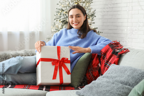 Happy young woman with Christmas gift box sitting on sofa in living room