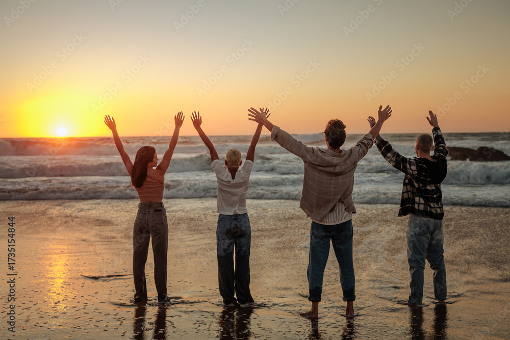 Fototapeta premium Friends raising arms enjoying golden sunset at beach