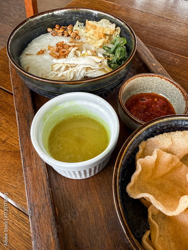 Wallpaper Mural Traditional Indonesian chicken porridge or Bubur Ayam served with crackers, chili sauce, green sauce, and toppings on a wooden tray over rustic wooden table. Torontodigital.ca
