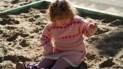 Child playing in sandy area wearing warm sweater on a bright sunny day outdoors