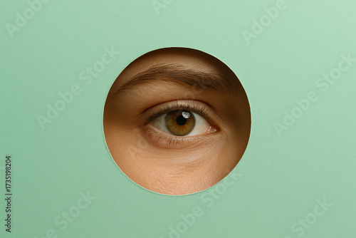 Wallpaper Mural Close up view of eye peering through circular cutout in green paper, creating striking visual effect. image conveys curiosity and intrigue, highlighting eye details and texture Torontodigital.ca