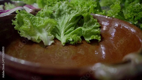 Close-up of a hand arranging green lettuce leaves inside a handcrafted clay dish. Symbol of traditional cooking methods, fresh food preparation, and homemade meals.