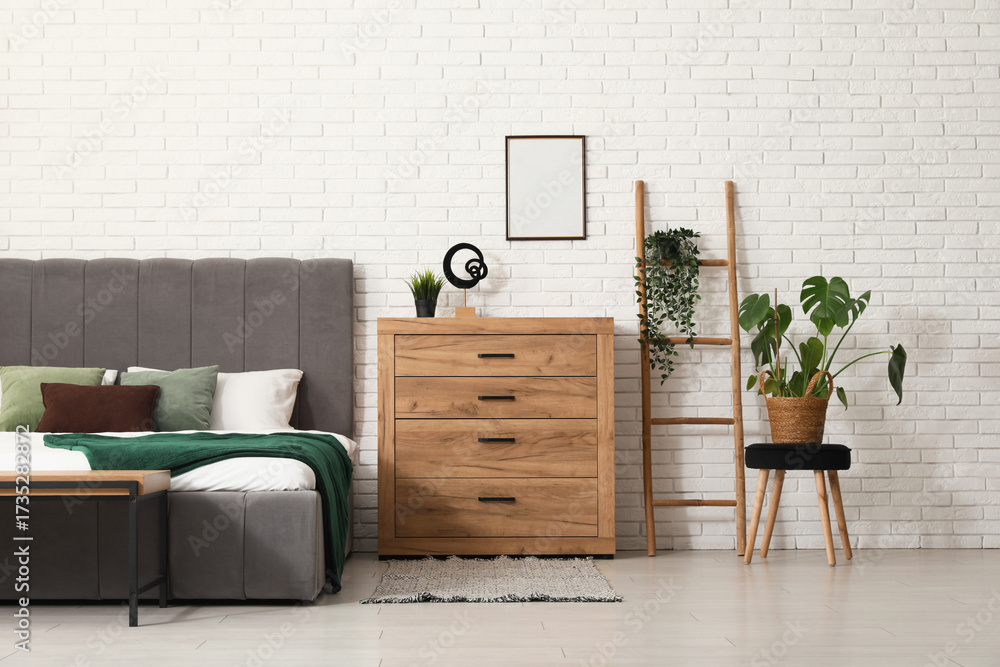 Fototapeta premium Bed, stepladder and chest of drawers near white brick wall in interior of bedroom