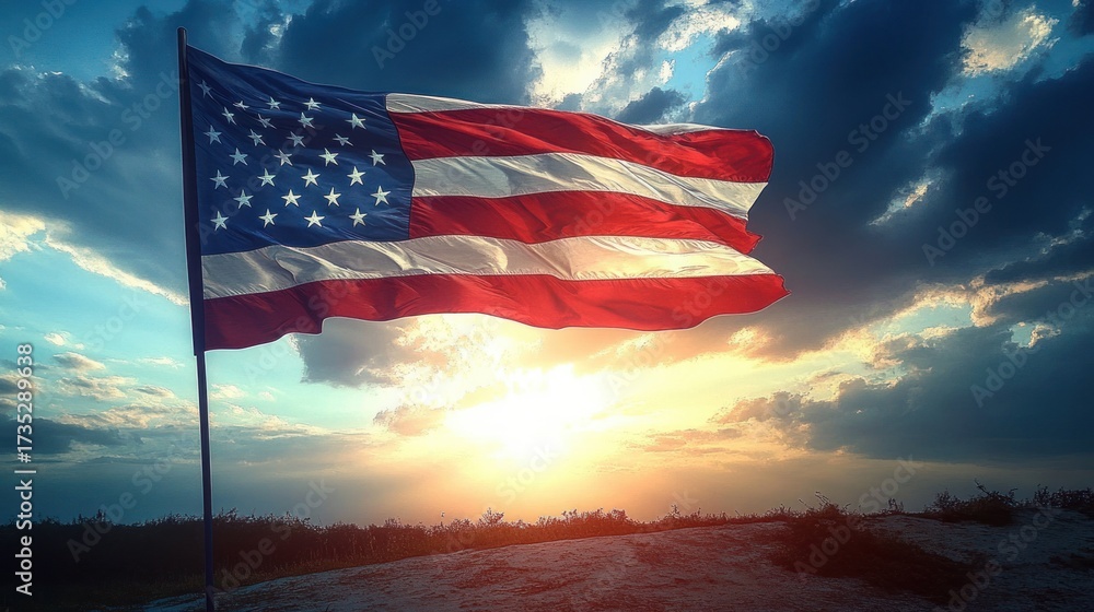 American flag waving on a pole with a dramatic sunset and cloudy sky in the background over a sandy landscape