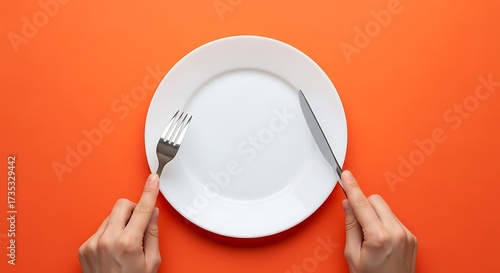 Empty white plate with cutlery on bright orange background overhead shot