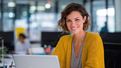A cheerful woman in a bright sweater engages with her laptop in a modern office environment. Free Download A cheerful woman in a bright sweater engages with her laptop in a modern office environment. - GFXLoad